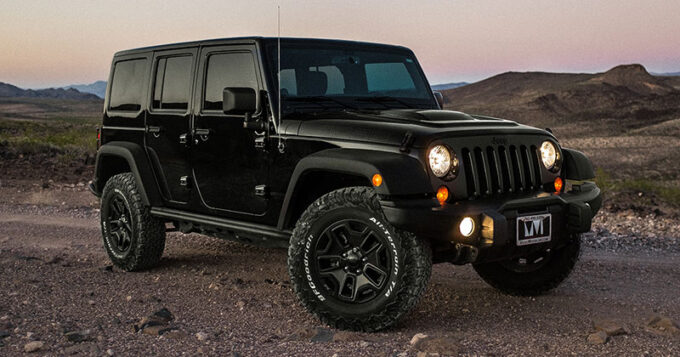 A black jeep wrangler in the desert at dusk with it's headlights on